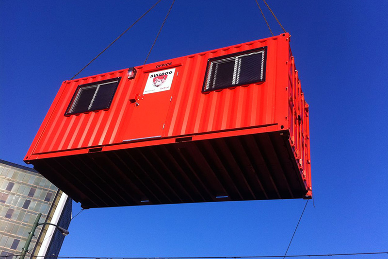 Shipping container office being lifted and moved by a crane.